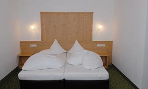 A simple bedroom with a double bed and wooden paneling. The walls are white and the room feels bright and spacious.