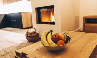 A cozy living atmosphere with a modern fireplace. On a wooden table lies a bowl of bananas and apples.