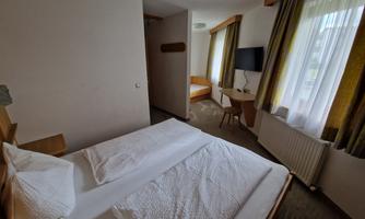 A simple hotel room with two single beds and a window. There is a television and a bright, friendly atmosphere.