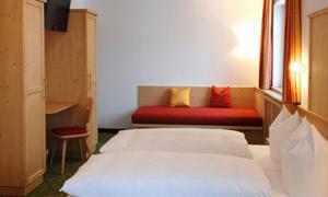 A cozy hotel room with two beds and a red sofa. The room features wooden furniture and a television.