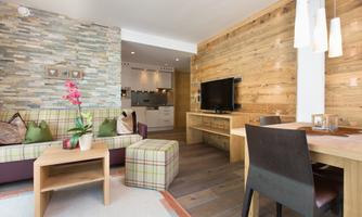 A modern living room with a cozy sofa, wood and stone elements. The space is bright and inviting, featuring a dining area and a TV console.