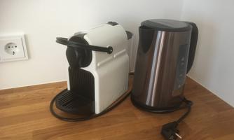 A white coffee machine stands next to a silver kettle on a wooden surface. Both appliances are ready for preparing beverages.