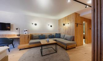 A modern living room with a comfortable seating arrangement and a wooden table. There is a television on the wall and soft lighting.