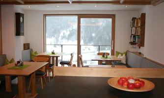 A cozy café with wooden interior and large windows overlooking a snowy landscape. Tables are decorated with green placemats and a fruit bowl.