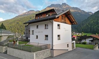 A charming building in the Alps with wooden cladding and a beautiful garden. The surrounding mountains and the green landscape give the place a tranquil atmosphere.