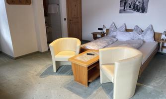 A simple room with a double bed, two cozy armchairs, and a wooden table. On the wall hangs a picture of five people.