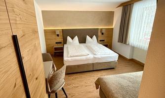 A modern hotel room with two single beds and light wooden details. Large windows provide plenty of daylight and a cozy atmosphere.