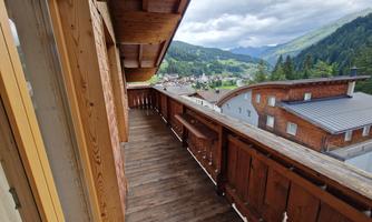 A wooden balcony overlooking a picturesque valley and mountains. The atmosphere feels calm and inviting.