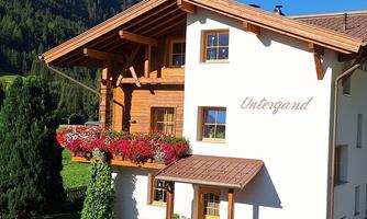 A charming building with wooden accents and colorful flower balconies. In the background, green mountains and trees are visible.