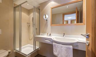 A modern bathroom with a shower, a sink, and a large mirror. The walls are light, and the decor is clean and functional.