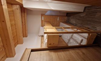 A cozy room with a wooden bunk bed. The walls are light and the floor has a modern design.