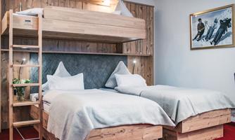 A cozy room with a bunk bed and two single beds. The walls are clad in wood and there are a couple of decorative pictures.