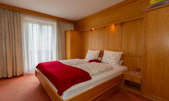 A cozy bedroom with a large double bed and wooden furniture. The windows let in plenty of light and create a bright atmosphere.