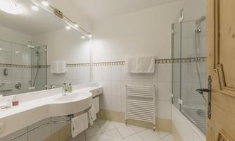 A modern bathroom with a large mirror and a glass shower. The walls are light-tiled, and there are fresh towels and toiletries.