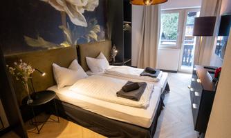 A modern bedroom with two beds and an elegant wall design. The room has large windows that let in plenty of daylight.