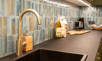 A modern kitchenette with an elegant faucet and a black sink. The walls are tiled with blue tiles that create a stylish atmosphere.