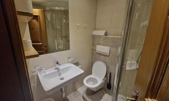 A modern bathroom with a shower, sink, and toilet. The walls are brightly tiled, and there is pleasant lighting.