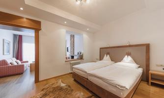 A modern hotel room with two single beds and a cozy seating area. The room is bright and inviting, with wooden flooring and natural light.
