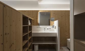 A modern bathroom with wooden walls and an elegant sink. Shelves provide storage space and a large mirror lighting creates a pleasant light.