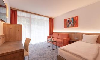 A modern hotel room with a single bed and a cozy seating area. Large windows provide plenty of natural light and create an inviting atmosphere.