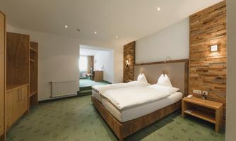 A modern hotel room with a double bed and wooden details. The room is bright and inviting, with a cozy carpet and soft lighting.