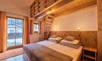 A cozy bedroom with wood decor and a double bed. Natural light enters the room through the windows.