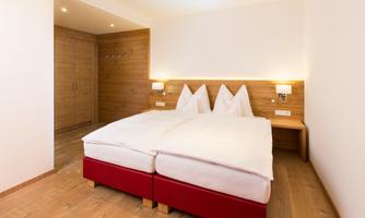 A modern bedroom with a double bed and wooden elements. The walls are bright and the lighting is cozy.