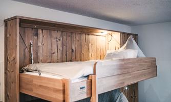 A comfortable wooden bunk bed in a modern room. The walls are designed with wooden paneling and there is soft lighting.