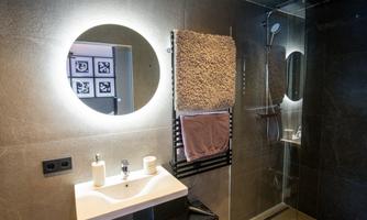 A modern bathroom with a round mirror and an elegant shower. Towels hang on a radiator, and the design is minimalist and stylish.