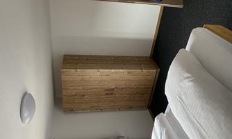 A cozy bedroom with two beds and a wooden wardrobe. The room has light walls and a carpeted floor.
