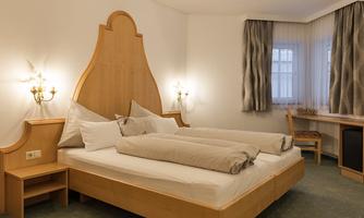 A cozy room with a double bed and light wood decor. The walls are in soft colors and the light is pleasant.