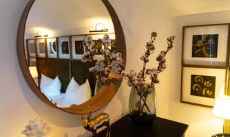 A stylish room with a round mirror and modern artworks on the wall. A plant and a golden decorative figure are on the table.