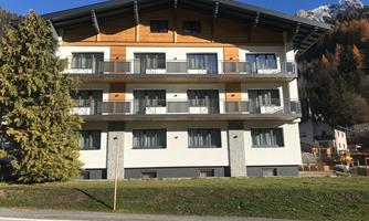 A modern building with wooden cladding and large windows. It is located in a mountainous area.