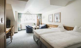 A cozy hotel room with two separate beds. There is a desk, an armchair, and plenty of space with natural light.