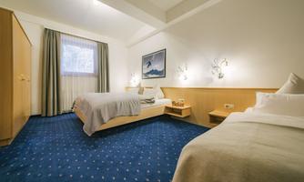 A cozy hotel room with two beds and blue carpets. The furnishings are bright and friendly, with a window and a decorative painting on the wall.