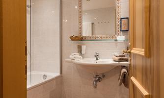 A modern bathroom with a bathtub and a shower. The walls are brightly tiled and there are fresh towels on the sink.