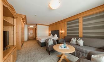 A modern hotel room with wooden furniture and a cozy seating area. There is a double bed and a table with a bottle of water.