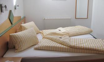 A simple bedroom with a double bed, striped bedspreads, and pillows. A small picture hangs on the wall, and a mirror is also present.