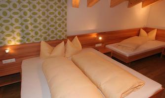 A cozy bedroom with two beds and large, comfortable pillows. The walls are decorated with a modern green pattern.