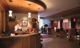 A cozy reception area with wooden paneling and warm lighting. A friendly staff member stands at the reception in traditional attire.