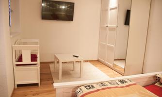 A modern room with a television, a coffee table, and a mirror. There is a bed and a small crib in the corner.
