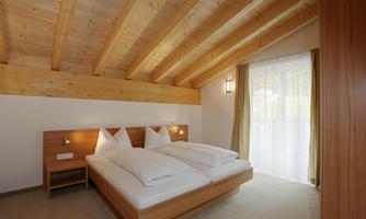 A modern bedroom with a wooden ceiling and two single beds. Large windows provide plenty of natural light.