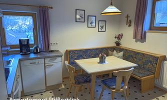 A cozy kitchen with a dining table and bench. Bright colors and windows create an inviting atmosphere.
