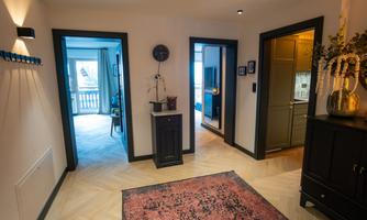 A bright hallway with three doors leading to different rooms. The floor is made of wooden planks, and a rug in warm colors lies in the entrance area.