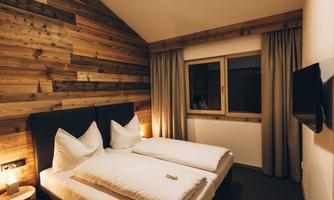 A cozy bedroom with a wooden wall design. There is a double bed, a window, and a television.
