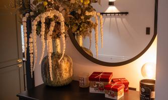 A stylish hallway with a round mirror and a large flower arrangement. On the table are decorative boxes and a lamp.