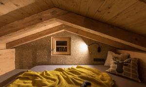A cozy loft with wooden beams and a window. On the bed lies a yellow blanket and a pillow.