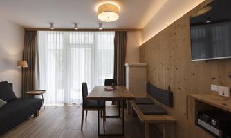 A cozy living space with wooden paneling and large windows. There is a table, chairs, and a sofa, as well as a television on the wall.