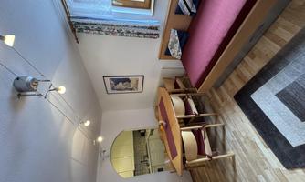 A cozy living room with a table and chairs as well as a sofa bed. The kitchen is visible through an open passage.