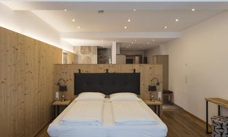 A modern room with a double bed and wooden accents. The lighting is soft and creates a relaxed atmosphere.